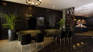 Un lobby moderno con un sofá de cuero, sillas negras, un gran reloj de pared y plantas en macetas.