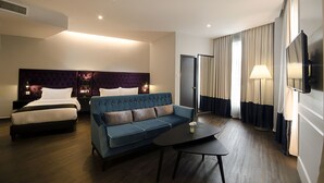 Una habitación de hotel con cama, sofá, mesa de centro, televisor y lámpara.