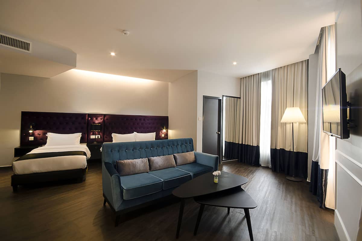 A hotel room with a bed, a sofa, a coffee table, a TV, and a lamp.