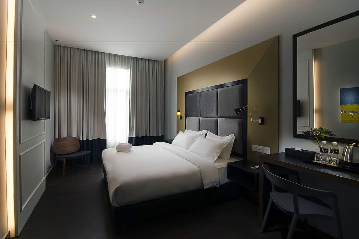 A hotel room with a large bed, a desk with a chair, a television, and a large window with curtains.