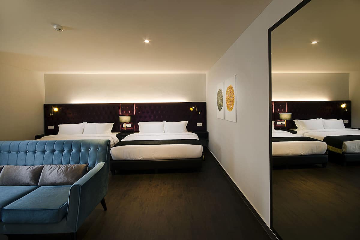 A hotel room with two beds, a blue sofa, and a large mirror.