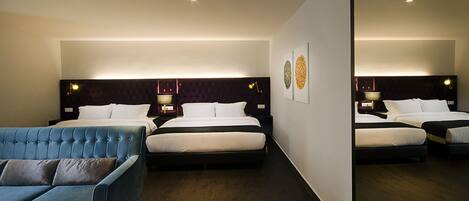 A hotel room with two beds, a blue sofa, and a large mirror.
