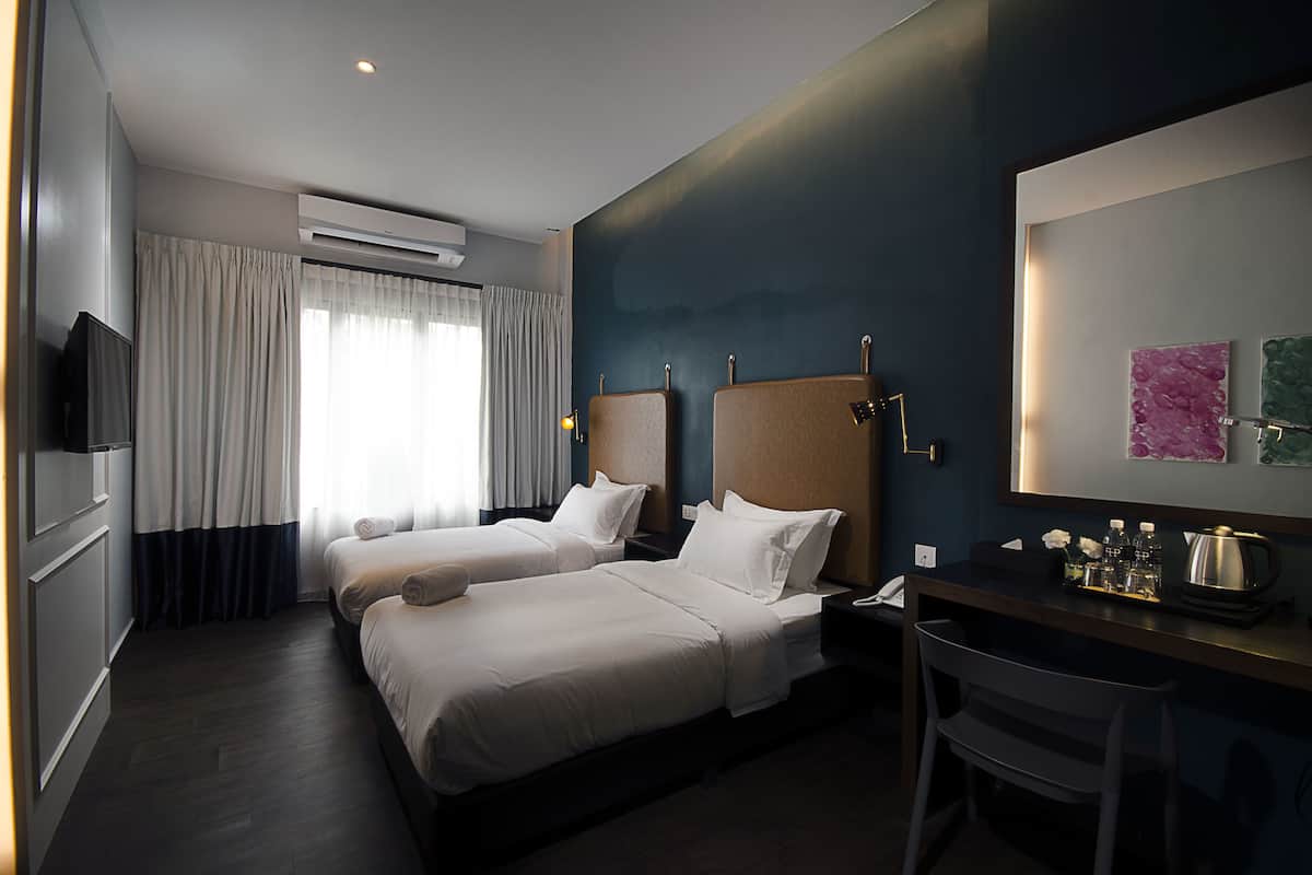 A hotel room with two beds, a desk with a chair, a television, and an air conditioning unit.