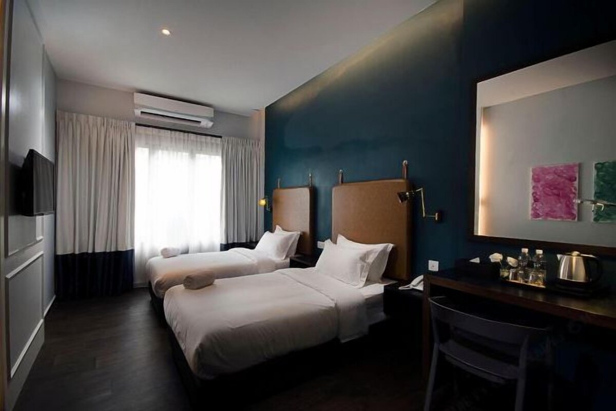 Habitación de hotel con dos camas, un escritorio, una silla, un televisor de pantalla plana y una ventana con cortinas.