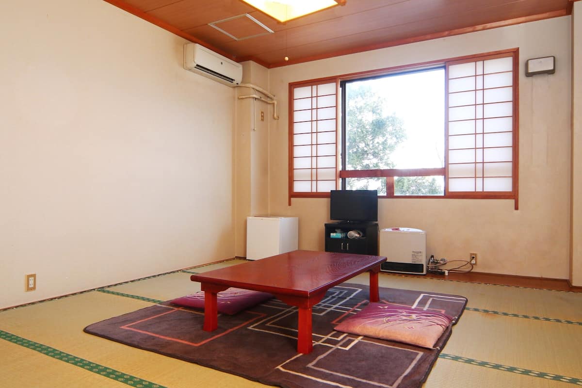 A tatami mat room with a low table, cushions, a heater, and a window with shoji screens.