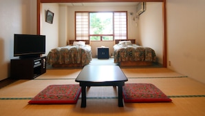 Une pièce de style japonais traditionnel, avec un sol recouvert de tatamis, une table basse, deux lits dotés de draps à motifs floraux et un téléviseur posé sur un meuble.