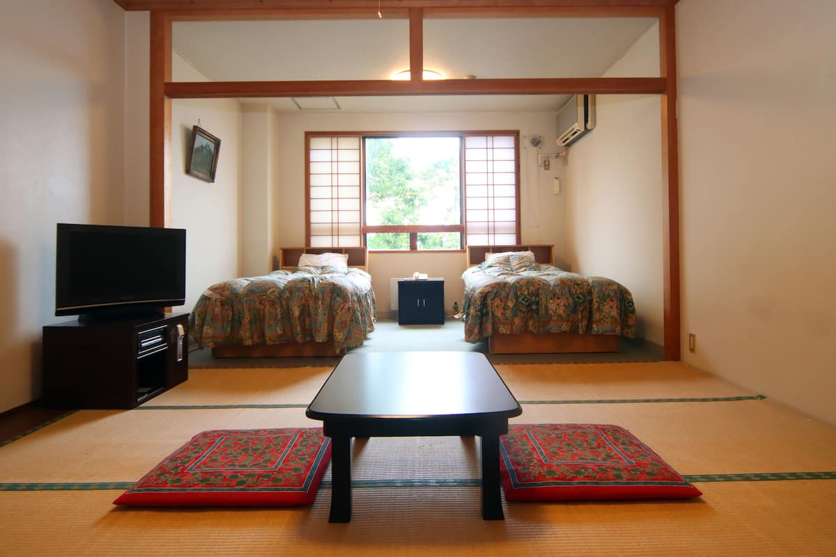A traditional Japanese-style room with tatami flooring, a low table, two beds with floral bedding, and a television on a cabinet.