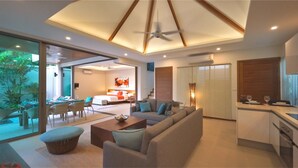 A modern living room with a sofa, coffee table, and dining area. There is a kitchen with a counter and a dining table. The room has a ceiling fan and recessed lighting. - Rawai Ka Villa with Private Pool (Rawai)