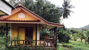 A two-story house with a balcony, surrounded by lush greenery and palm trees. - Sang Un Bungalow (Ko Yao)
