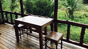 A wooden deck with a table and bench, overlooking a lush green landscape with various trees and a distant hill. - Sang Un Bungalow (Ko Yao)
