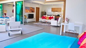Una sala moderna con un sofá azul grande, muebles blancos y una cocina al fondo.