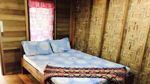 A wooden cabin-style room with a bed, a window with a pink curtain, and a woven wall panel. - Janya Homestay (Ko Yao)