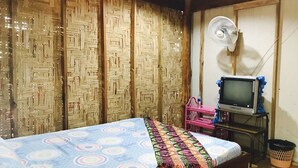 A room with a bed, a television on a stand, a fan, and a woven partition. - Janya Homestay (Ko Yao)