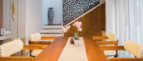 A dining area with a wooden table, white chairs, and a potted orchid.