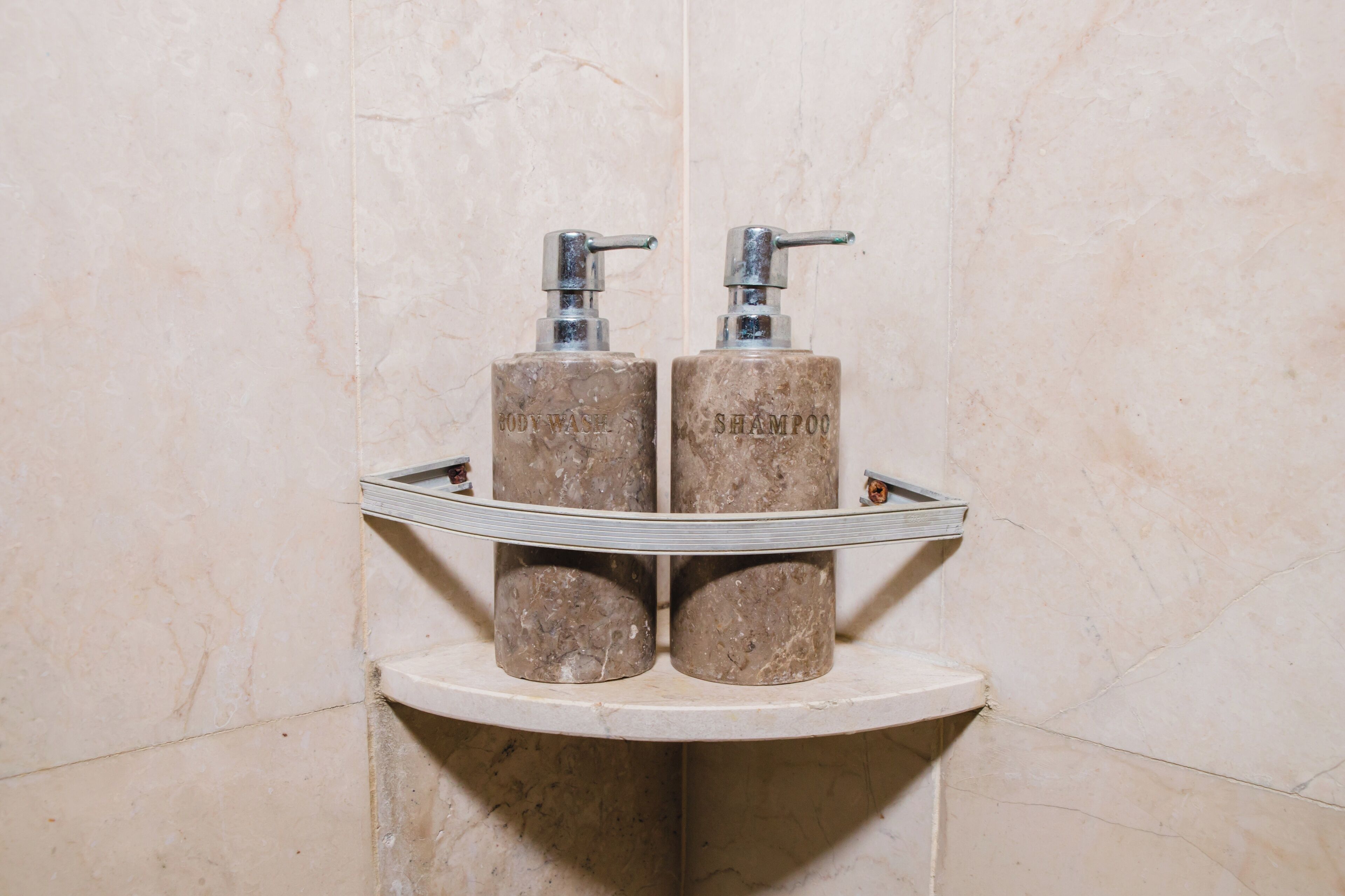 A bathroom with two cylindrical dispensers labeled "BODY WASH" and "SHAMPOO" on a marble countertop.