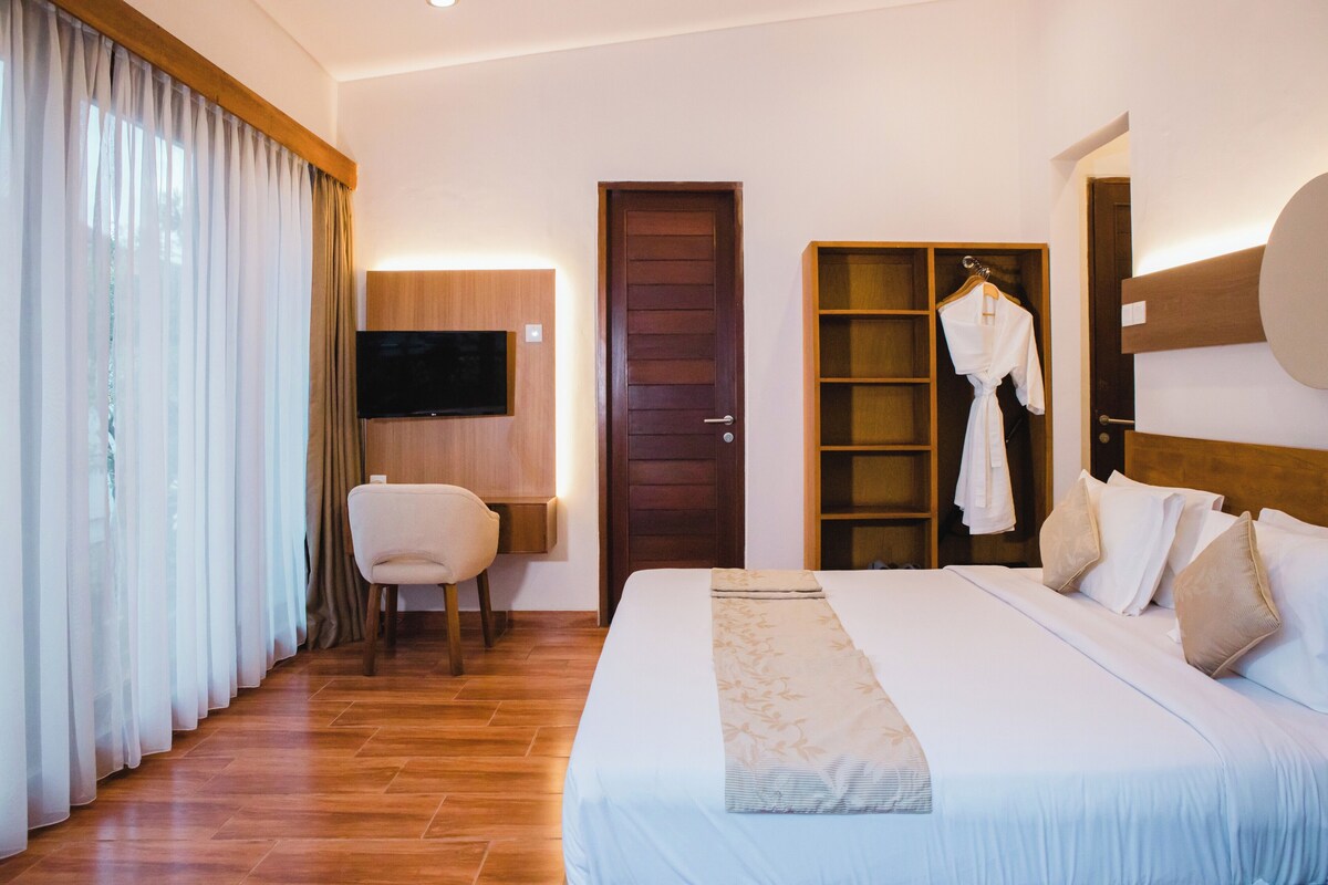 Une chambre d’hôtel avec un grand lit, une armoire en bois, un téléviseur fixé au mur et une chaise.