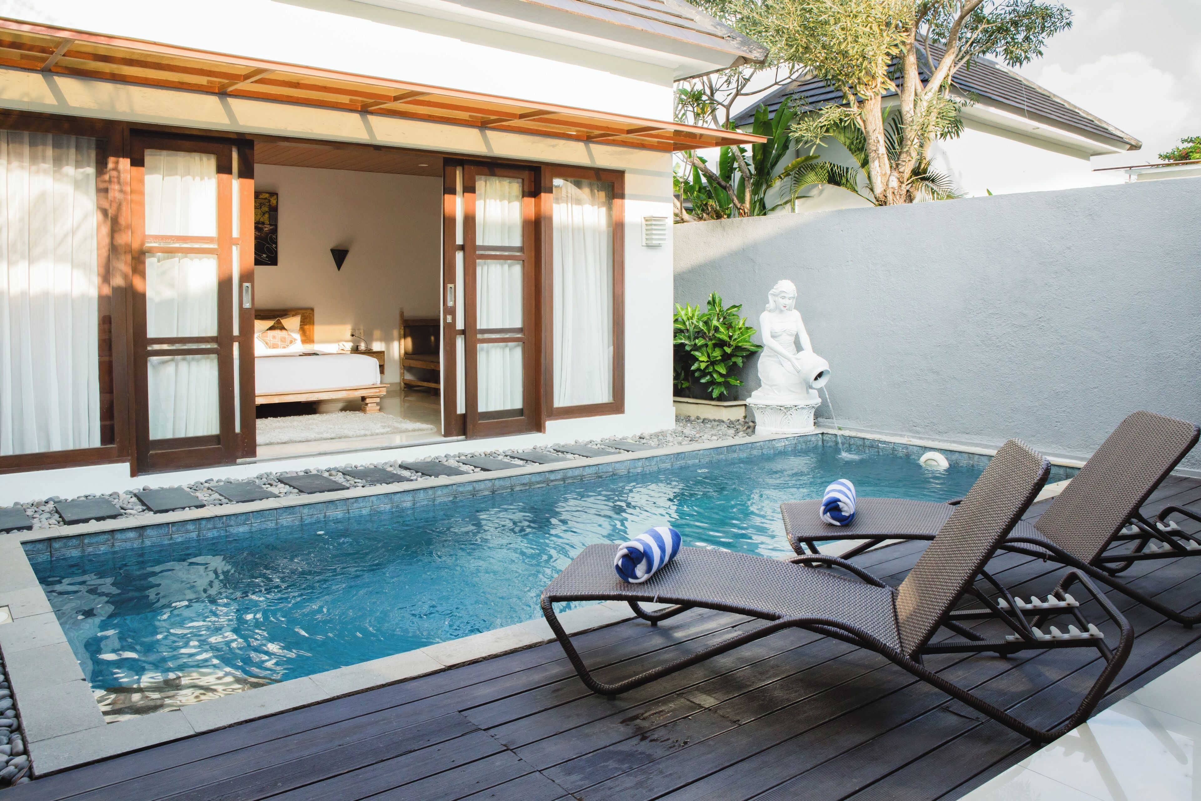 A poolside area with lounge chairs, a small pool, and a bedroom with a bed and curtains.