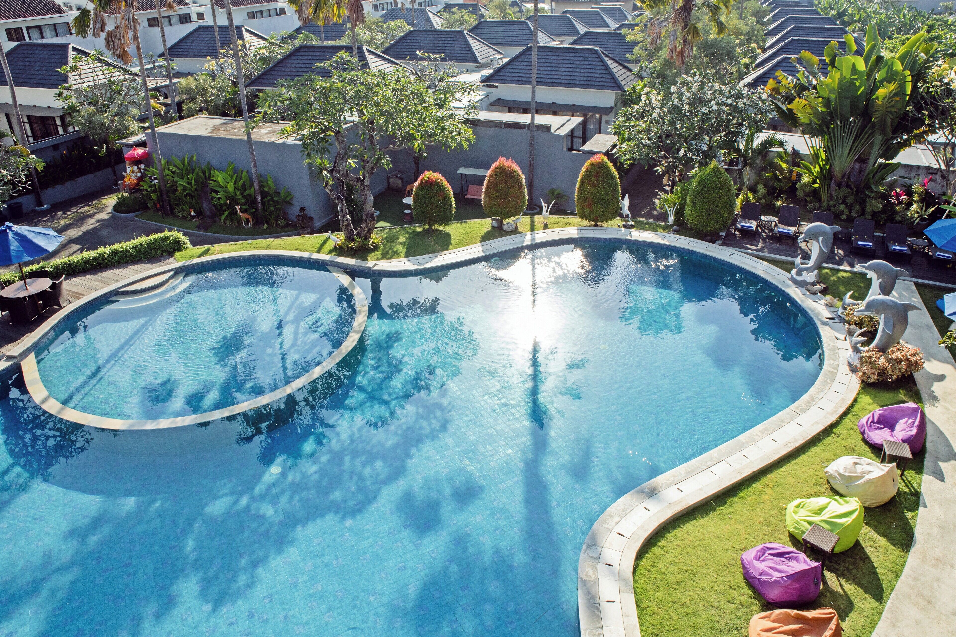 Una piscina de borde curvo, rodeada de césped y pequeños árboles.