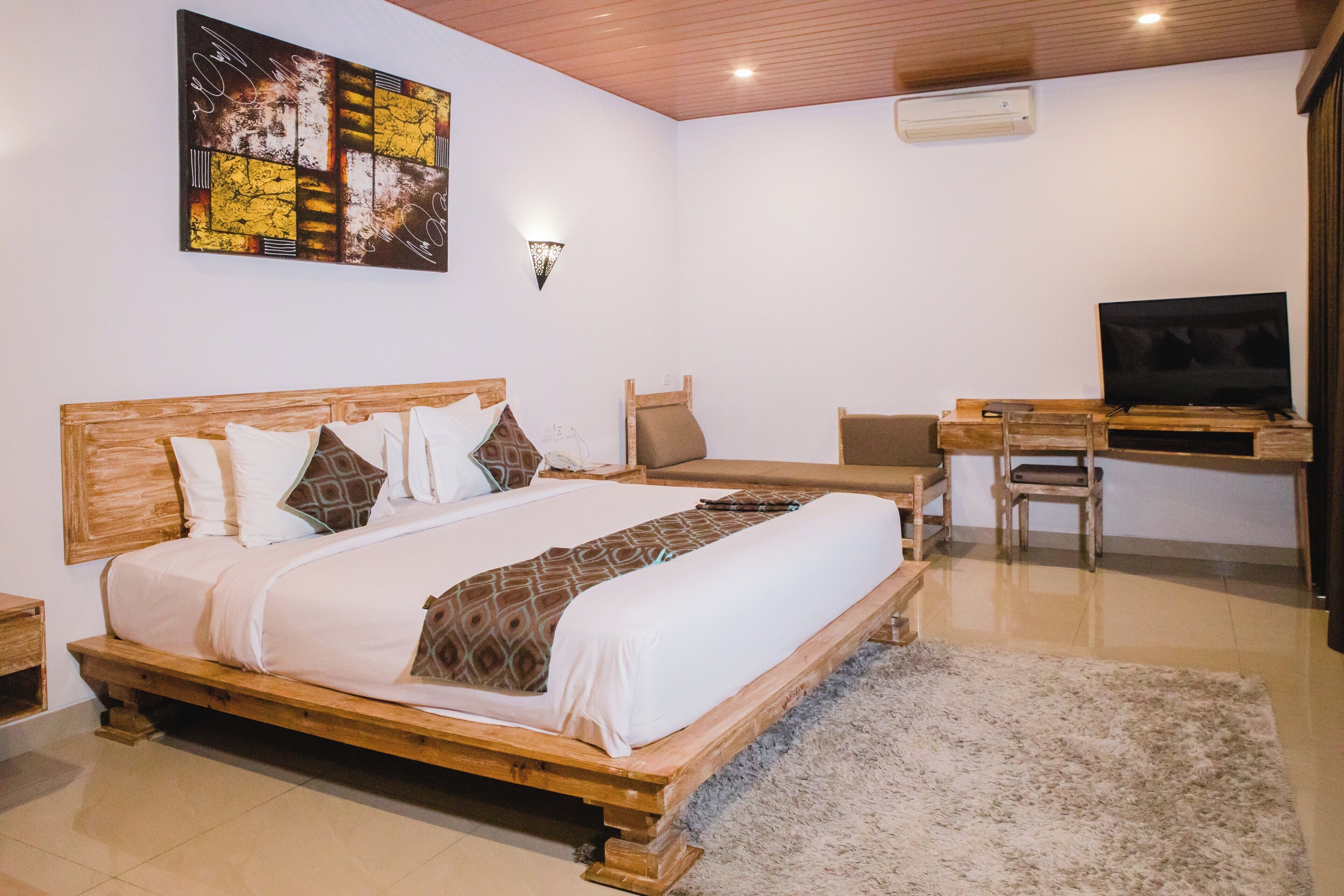A bedroom with a wooden bed, a desk, a television, and a wall-mounted air conditioner.