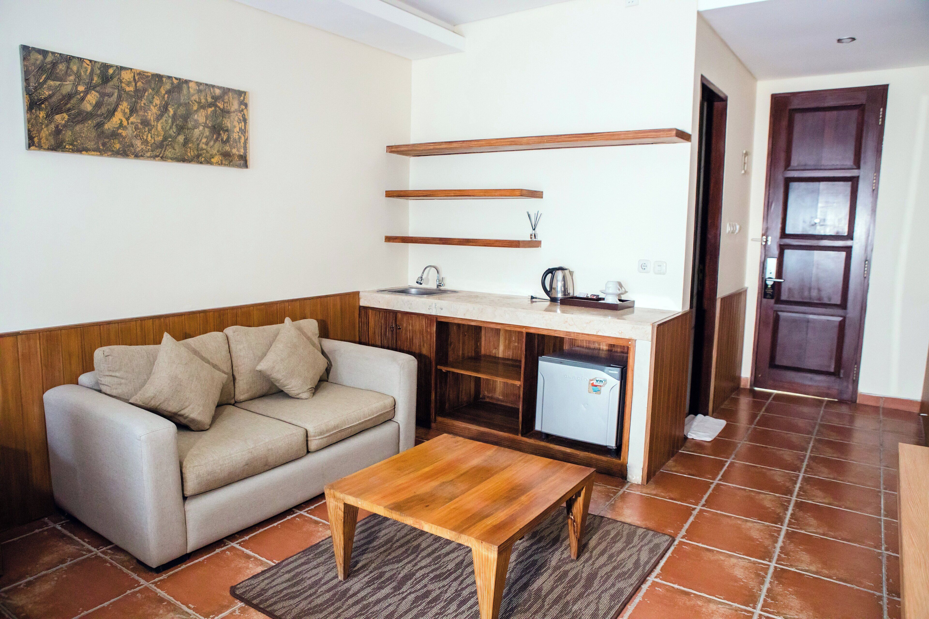 A living room with a sofa, a coffee table, a kitchen area with a refrigerator, and a wooden door.