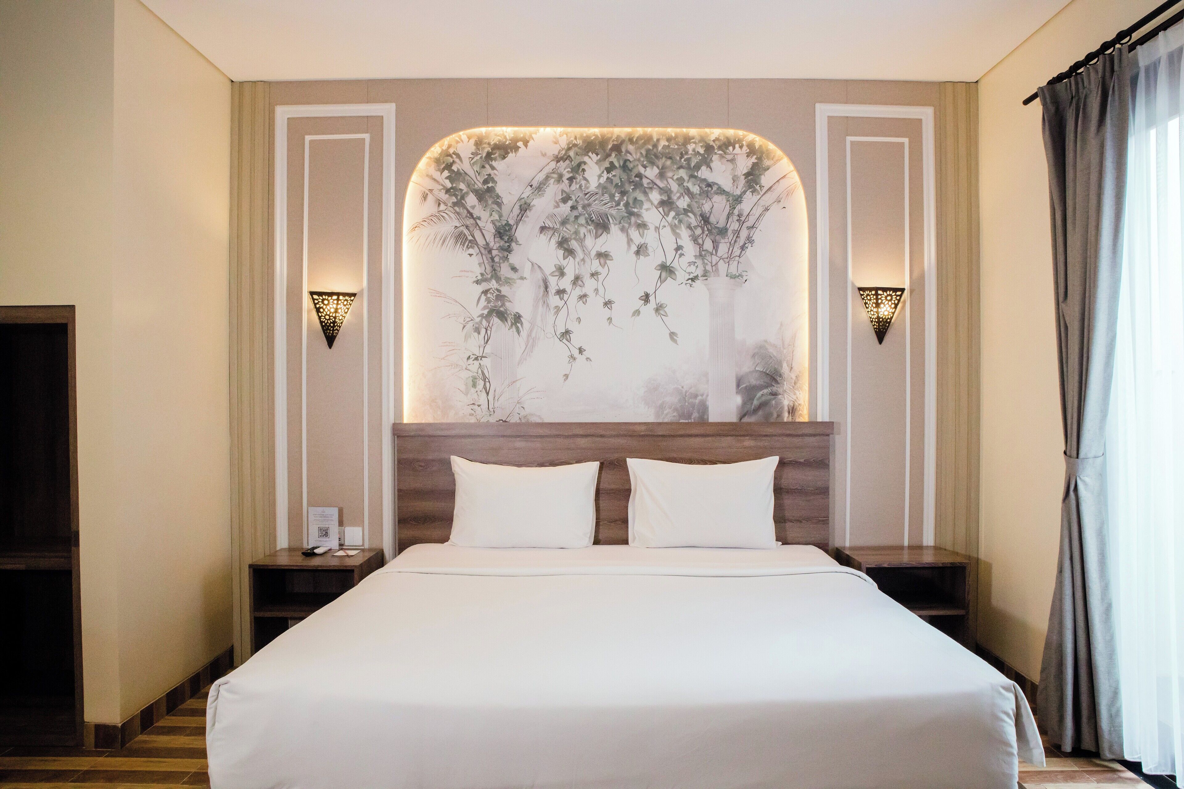 Une chambre d’hôtel avec un grand lit, deux tables de chevet, un luminaire fixé au mur et un rideau à la fenêtre.