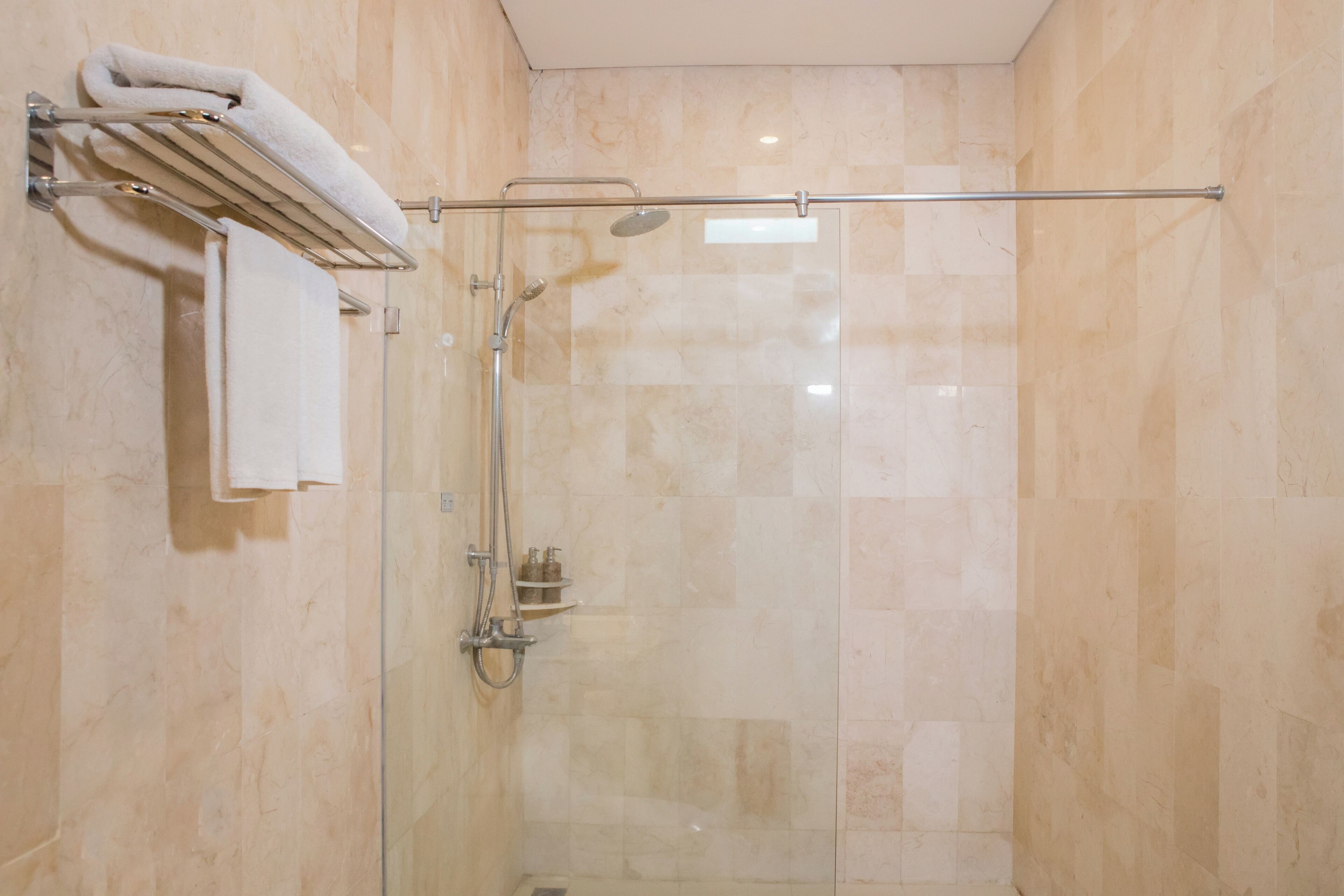 A glass-enclosed shower with a towel rack and a handheld showerhead.