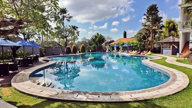 Una gran piscina amb un disseny circular, envoltada d'un jardí ben cuidat i diverses plantes tropicals.