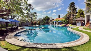 A large, clear swimming pool with a circular design, surrounded by a well-maintained lawn and various tropical plants. - Grand Kesambi Resort & Villa Bali (Kerobokan)