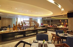 A hotel lobby with a buffet area, seating arrangements, and a large television screen.