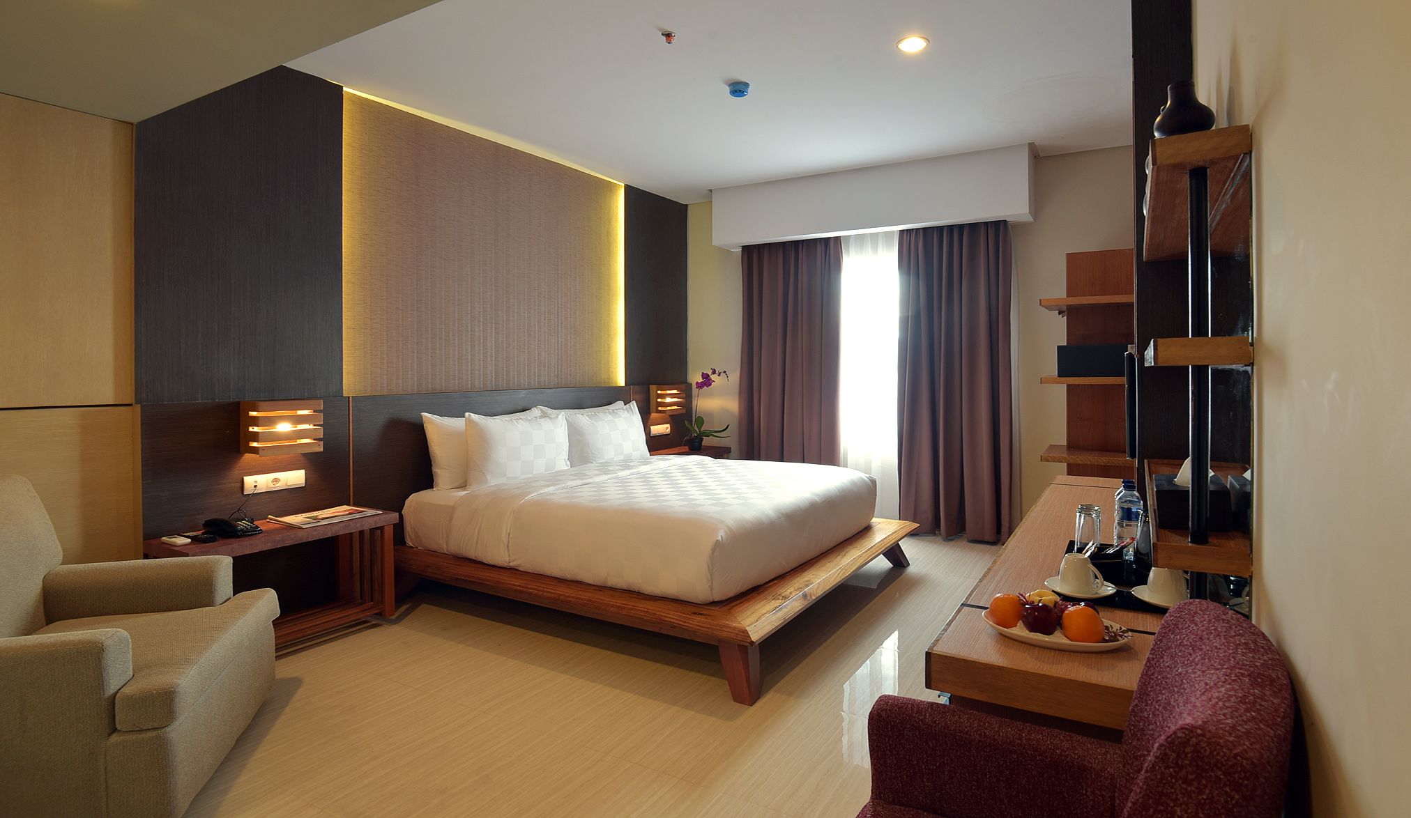 Een moderne hotelkamer met een groot bed, nachtkastjes, een bureau met een stoel en een klein zithoekje.