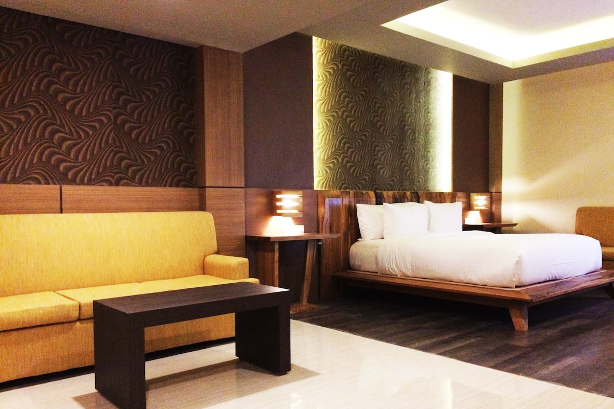 A hotel room with a sofa, a bed, a nightstand, and a lamp.