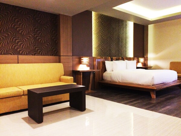 A hotel room with a sofa, a bed, a nightstand, and a lamp.