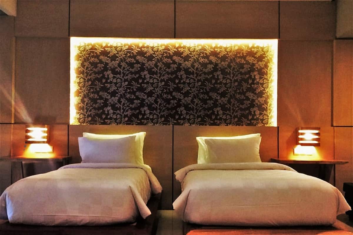 A hotel room with two beds, a floral wall panel, and bedside lamps.