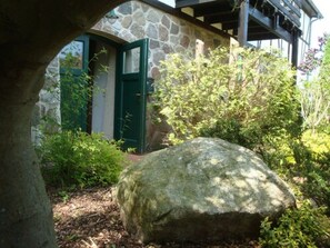 A stone building with a green door, surrounded by greenery and a large rock. - Gutspark Seeblick (Bastorf)