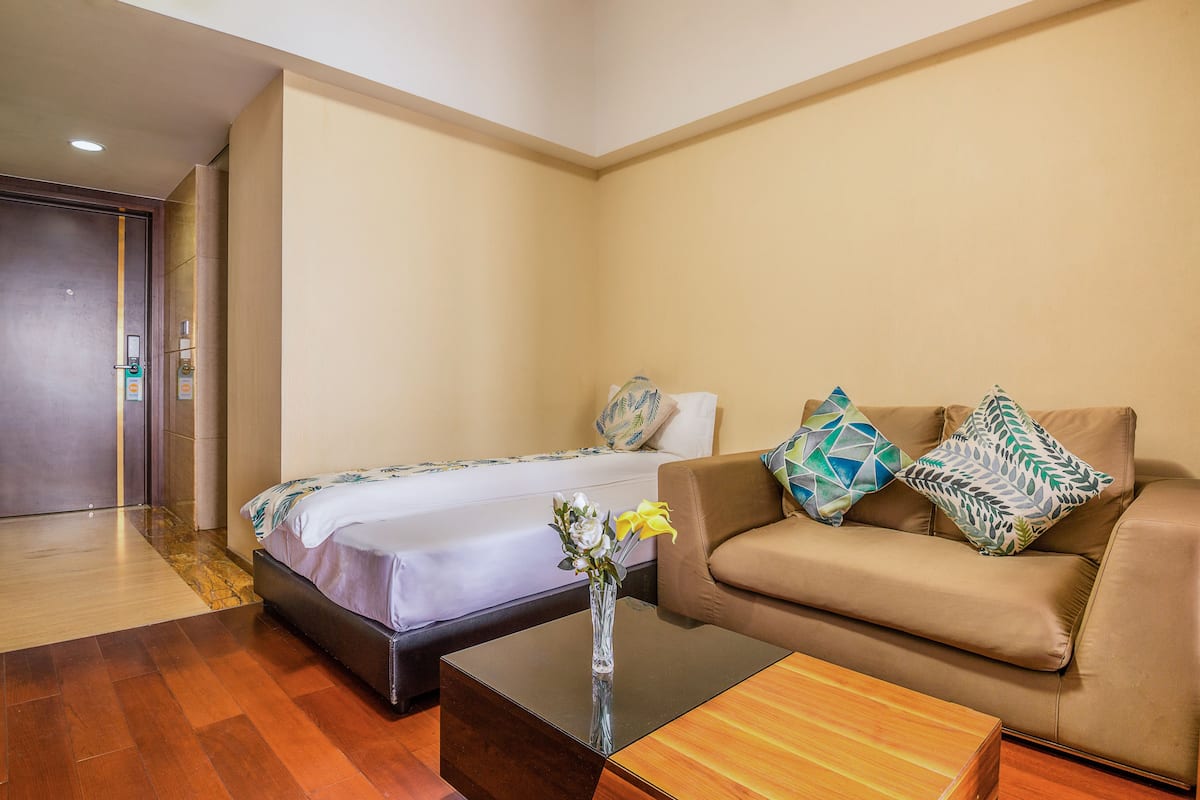 A hotel room with a bed, a sofa, a coffee table, and a vase with flowers.