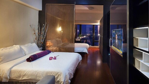 A modern hotel room with a large bed, a desk, and a view of the city at night. - Waifiden Apartment Pazhou Complex (Guangzhou)