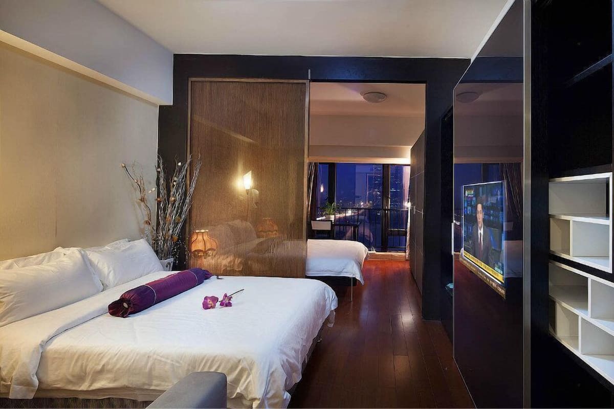 A modern hotel room with a large bed, a desk, and a view of the city at night.