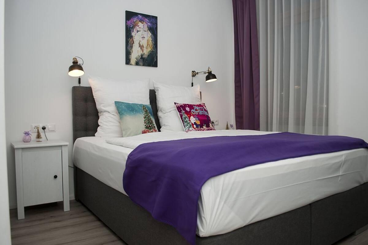 Ein modernes Schlafzimmer mit einem Bett, zwei Nachttischlampen, einem Nachttisch und einem Bild an der Wand.
