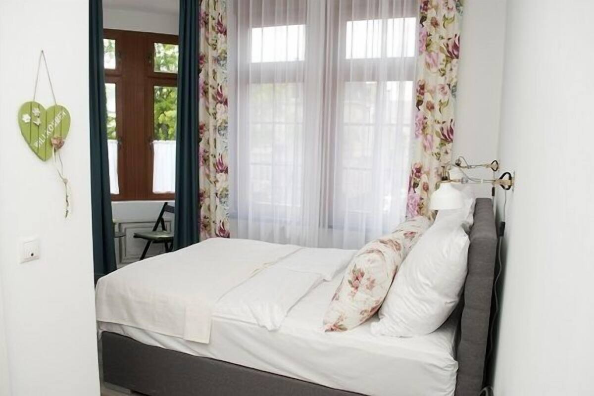 Ein Schlafzimmer mit einem Bett, floralen Vorhängen und einer herzförmigen Dekoration an der Wand.