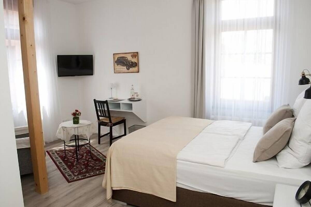 Ein Schlafzimmer mit einem Bett, einem Schreibtisch, einem Stuhl, einem Fernseher und einem Fenster mit Vorhängen.