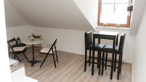 A small, well-lit room with a sloped ceiling, a round table with two chairs, a radiator, and a window with a view. - Residenz Hotel Garni Edenkoben (Edenkoben)