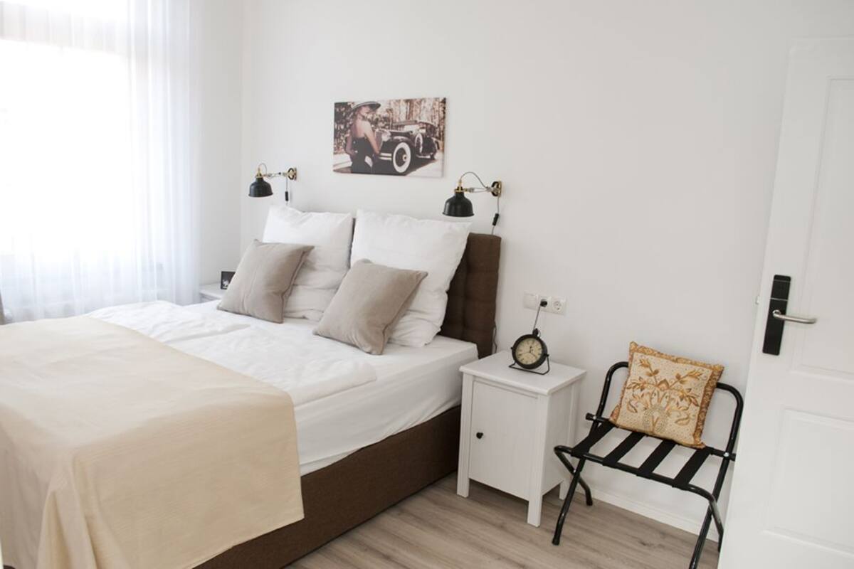 Ein ordentlich eingerichtetes Schlafzimmer mit einem Bett, Nachttischen, einer Uhr und einem Sessel.