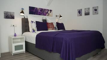 Un dormitorio con cama, mesita de noche blanca y decoración en la pared.