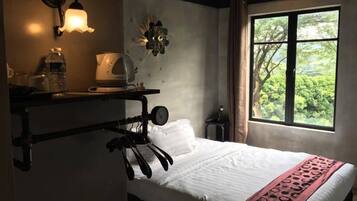 A bedroom with a bed, a shelf with a kettle, a water bottle, and a wall-mounted light fixture.