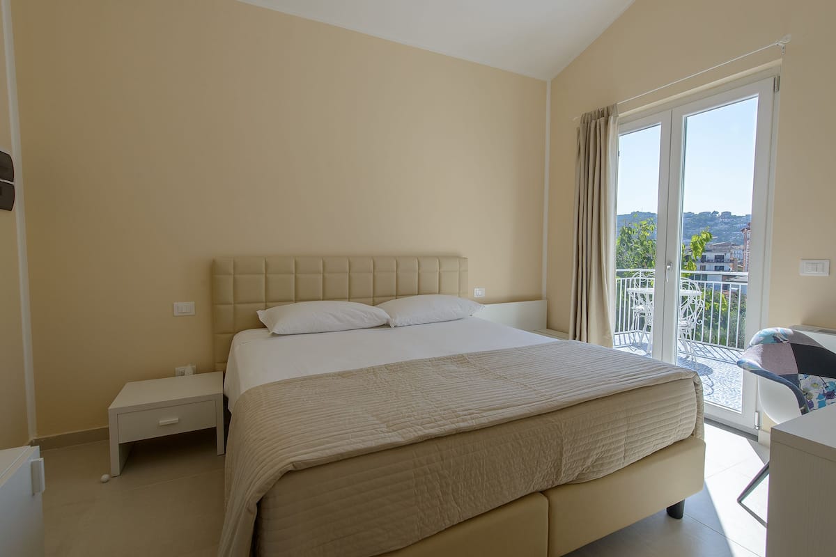 Ein Hotelzimmer mit einem großen Bett, einem kleinen Nachttisch und Blick auf den Balkon.