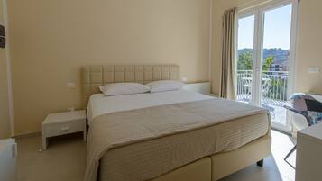 Habitación de hotel con una cama grande, una mesita de noche pequeña y vistas al balcón exterior.