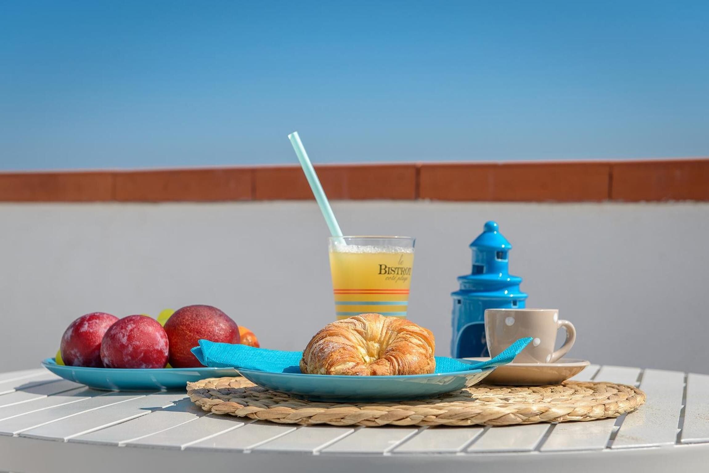 Desayuno con un croissant, manzanas y un vaso de zumo de naranja sobre una mesa con vistas al cielo.