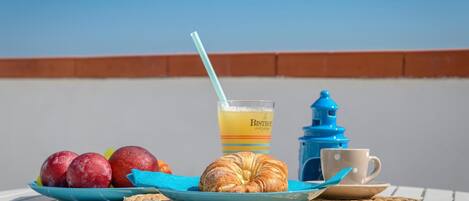 Desayuno con un croissant, manzanas y un vaso de zumo de naranja sobre una mesa con vistas al cielo.