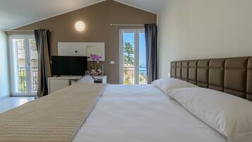 A hotel room with a large bed, a desk with a television, and a balcony with curtains.