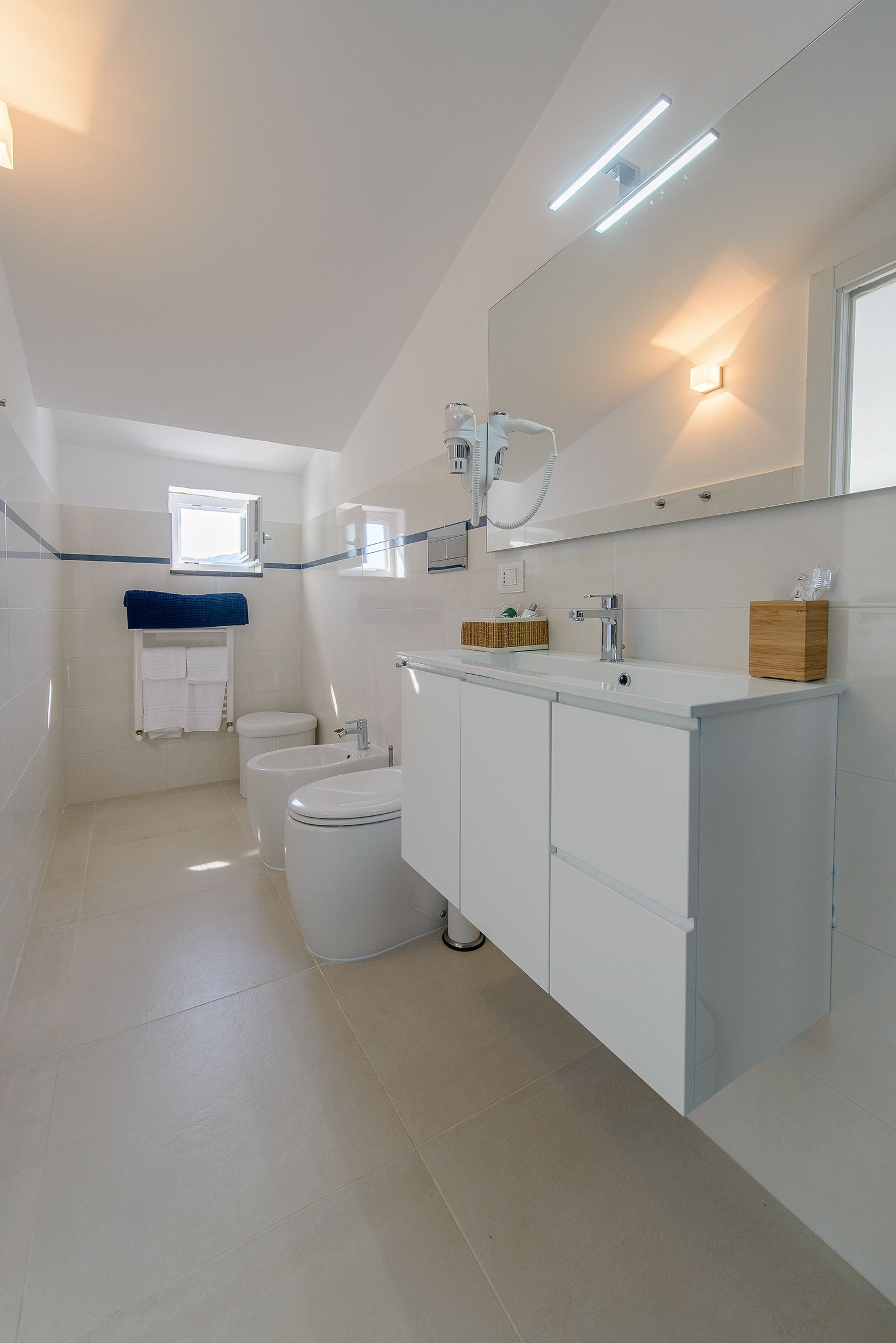 A modern bathroom with a white sink, vanity, and two toilets.